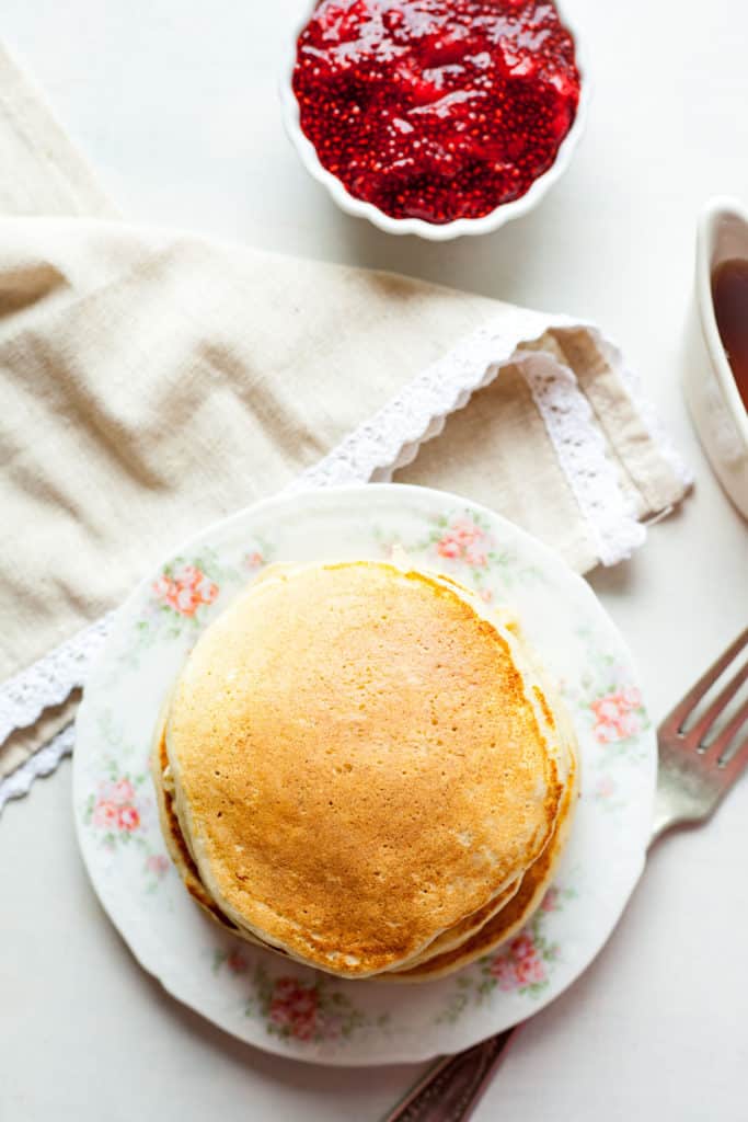 a stack of ricotta pancakes on a flowered plate with a fork and napkin.