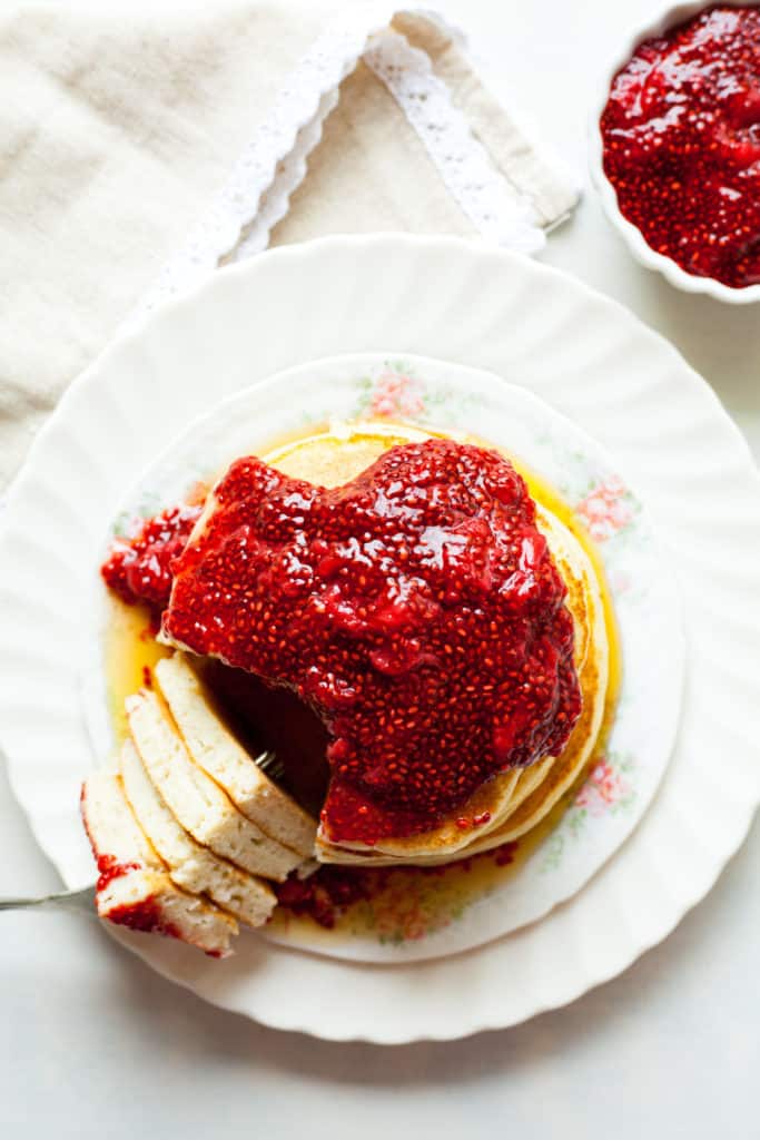 a stack of pancakes topped with jam and a forkful cut out.